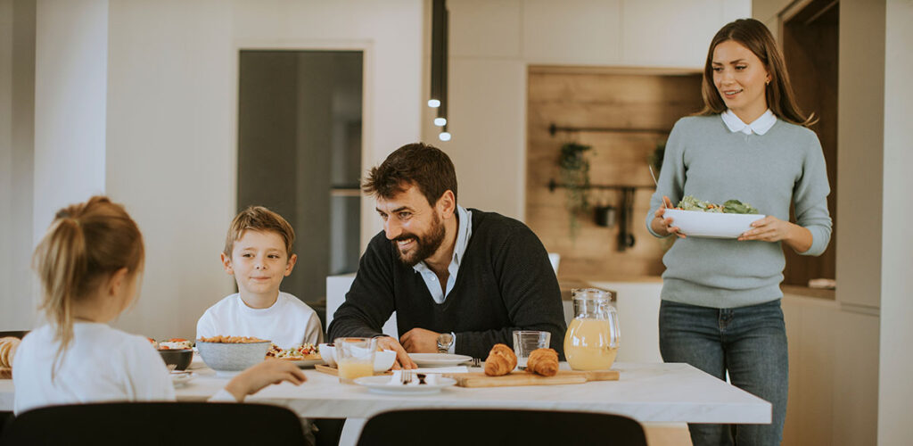 Family sitting down to breakfast at dining room table in luxury home