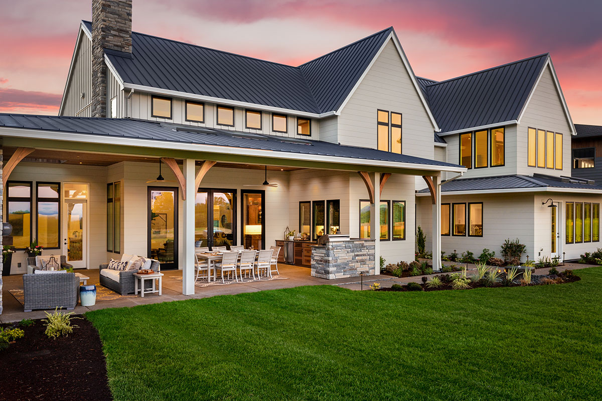 Beautiful luxury home exterior at sunset. Features large covered patio with outdoor furniture, barbecue, and table with chairs.