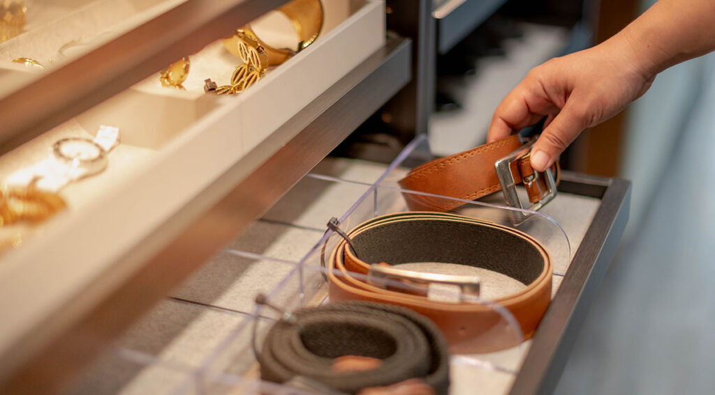 Female hand choosing the roll leather belt in the drawer shelf in a luxury closet in a luxury home.