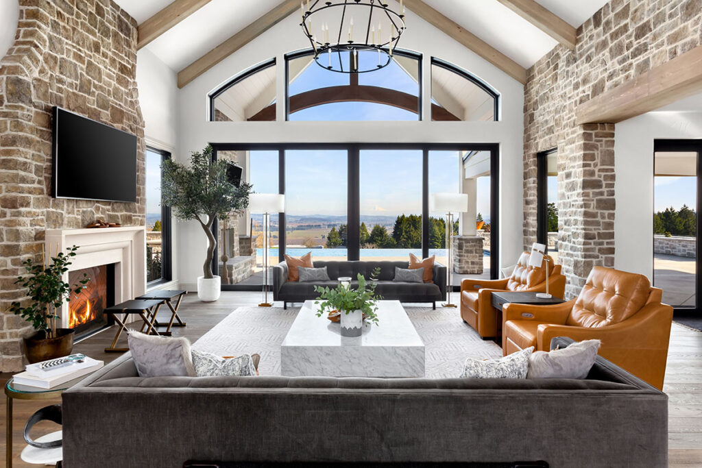 Beautiful living room in new traditional luxury home. Features stone accents, vaulted ceilings, fireplace with roaring fire, and gorgeous exterior view of infinity pool and valley.